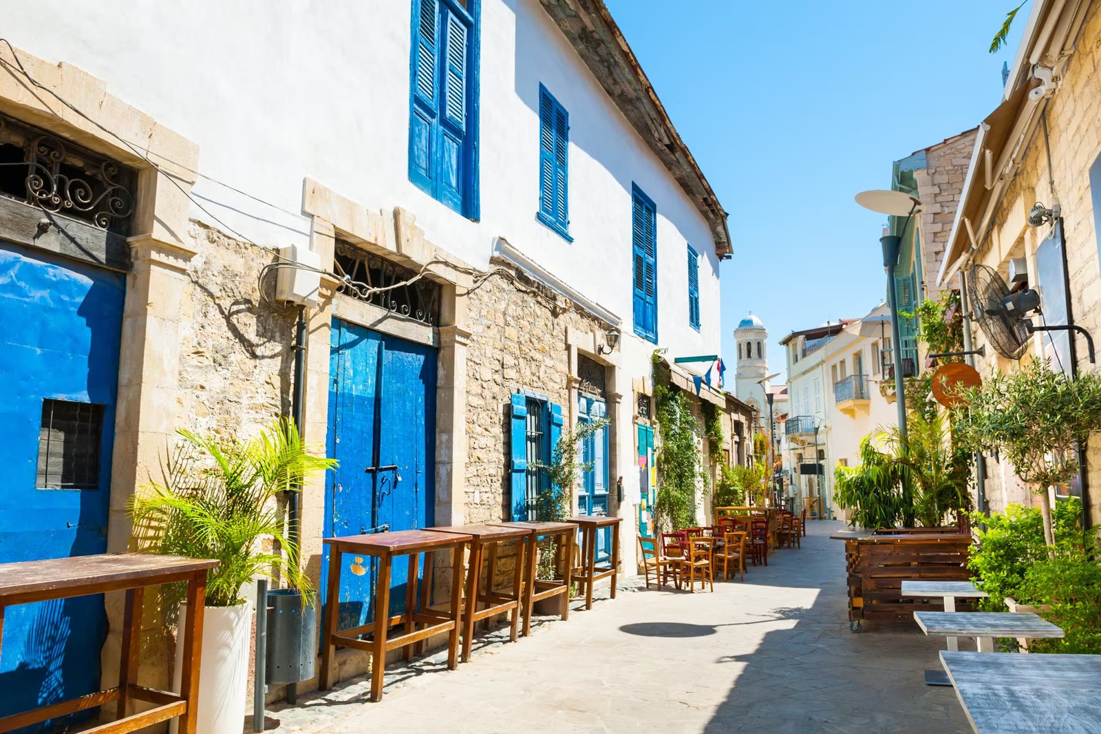 A narrow Limassol Old Town street with bright blue shutters and taverna tables